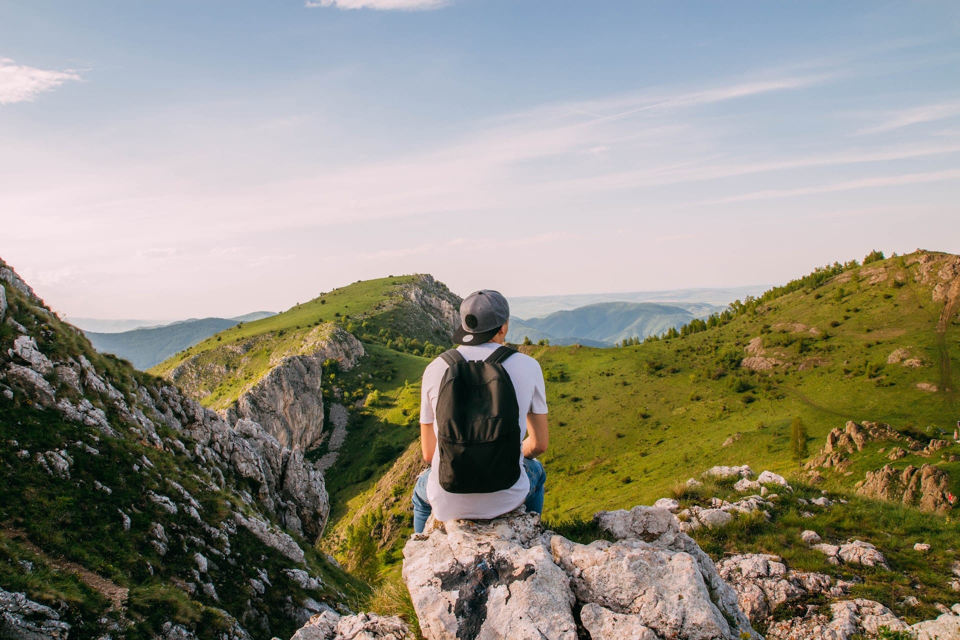 man-sitting-on-rock-facing-the-grass-covered-mountains