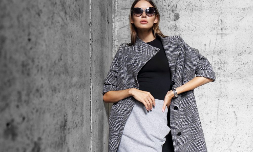 high fashion portrait of young elegant woman outdoor. Grey сoat, cat eye sunglasses, grey wall background