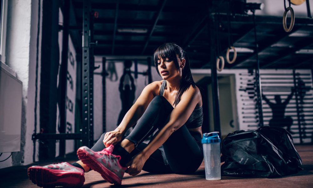 Fit athlete young woman tying shoe laces in the gym.