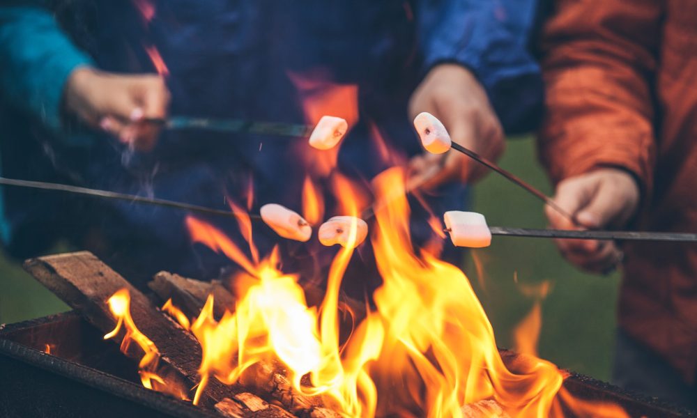 Hands of friends roasting marshmallows over the fire in a grill closeup