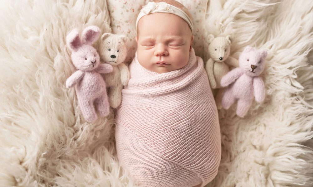 Cute newborn baby girl lies swaddled in a white blanket with toy