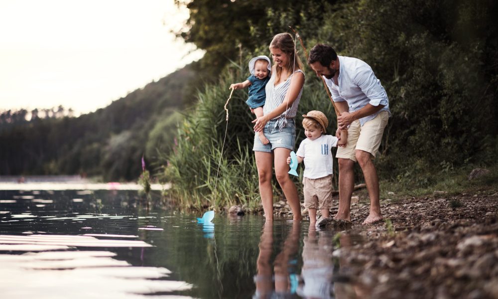 A young family with two toddler children spending time outdoors by the river in summer.