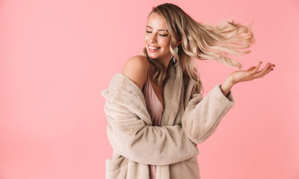 Image of a pretty woman posing isolated over pink wall background dressed in fashion coat shaking hair.