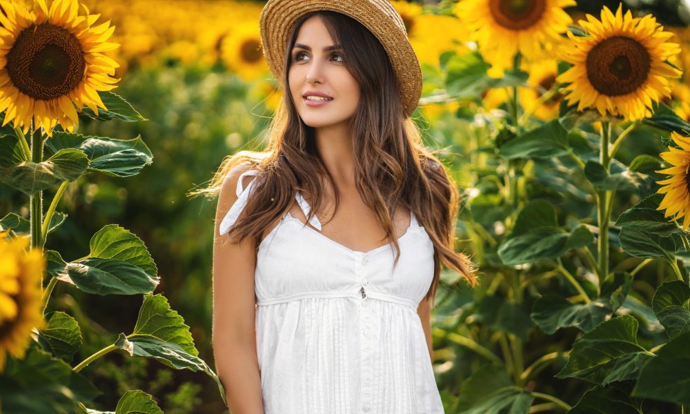 Young woman in white dress and straw hat on the field on a sunny day.