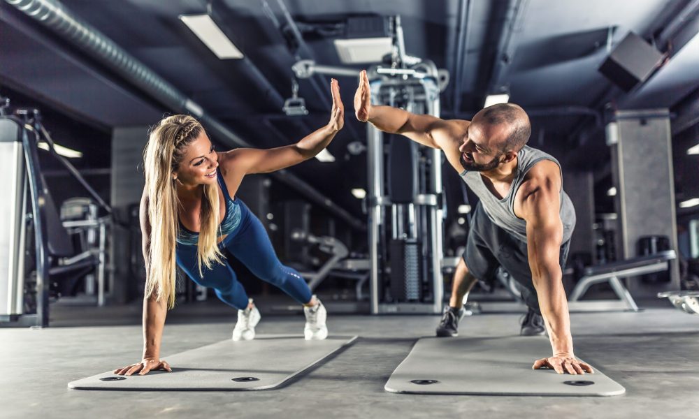 Sport couple doing plank exercise workout in fitness centrum. Man and woman practicing plank in the gym.
