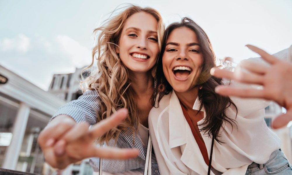 Lovable caucasian girls expressing positive emotions to camera. Outdoor photo of refined sisters posing on sky background.