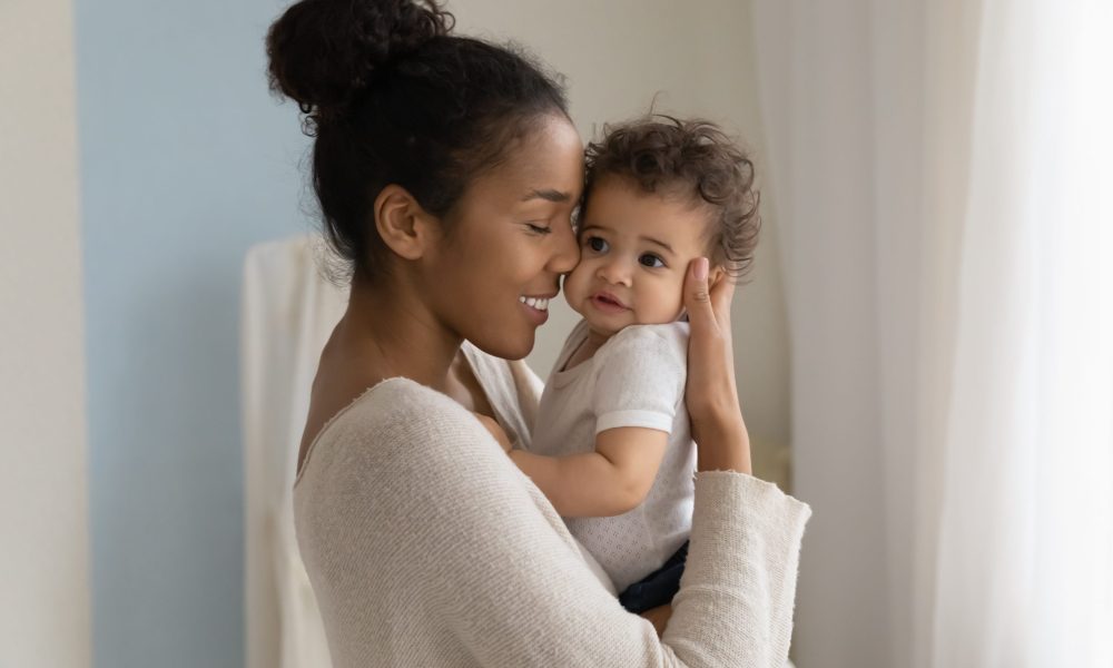 Happy young African American mom hold in hands hug cute little ethnic baby toddler show love care. Smiling biracial mother embrace cuddle small newborn infant child. Motherhood, childcare concept.