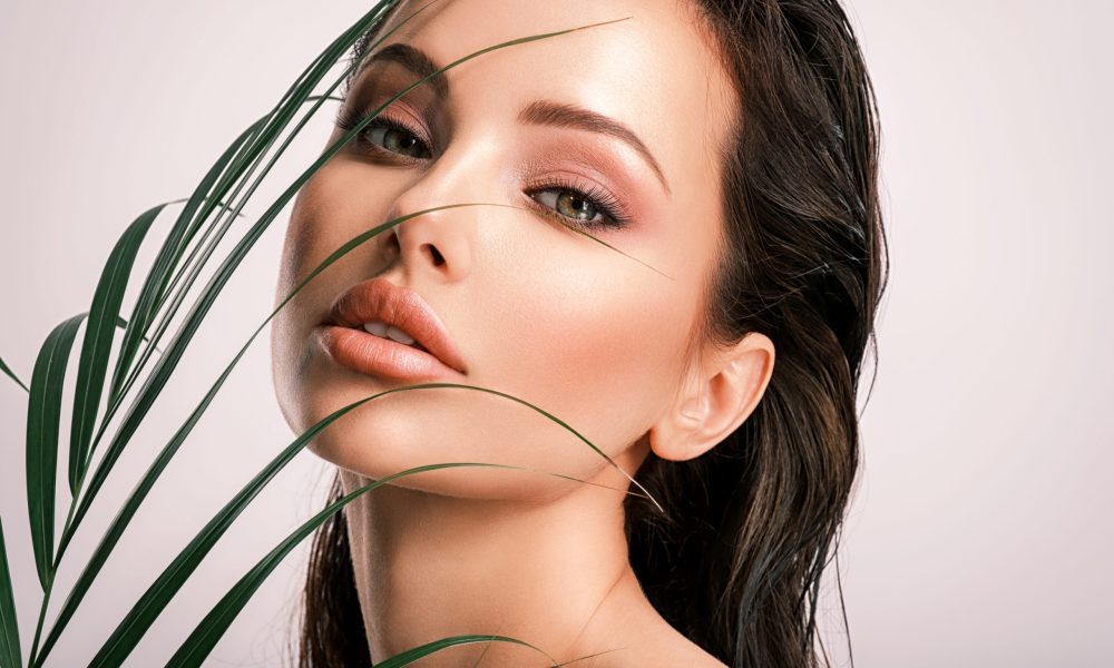Young beautiful woman with green leaves near face and body. Skin care beauty treatments concept.  Closeup girl's face with green leave. White model with clean, health skin of face - posing at studio
