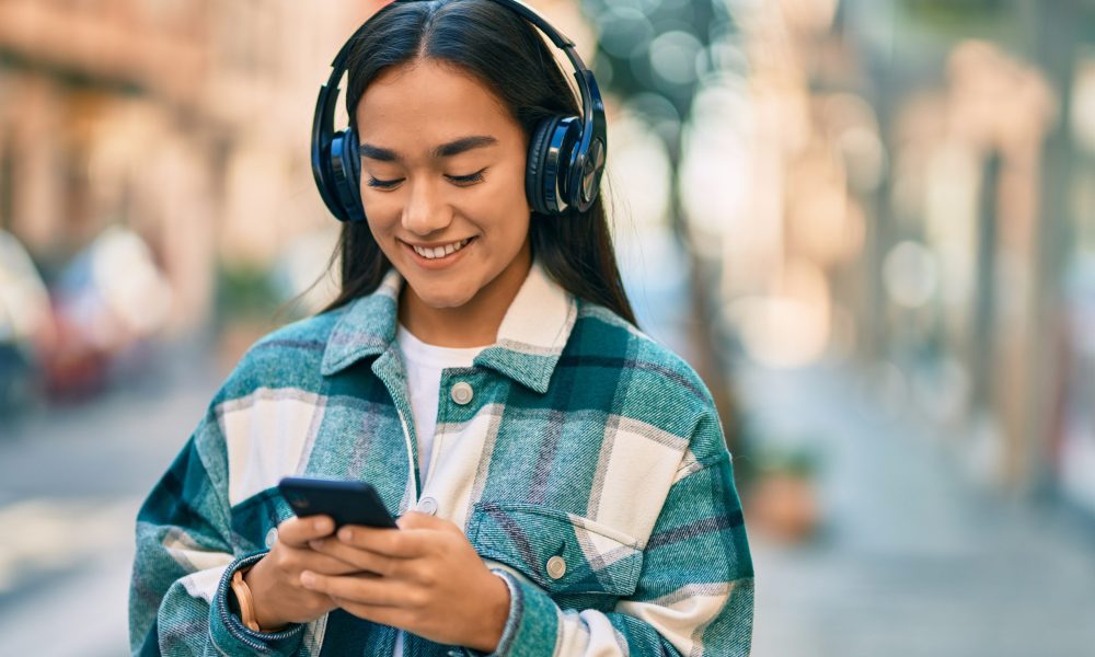 Young latin girl smiling happy using smartphone and headphones at the city.
