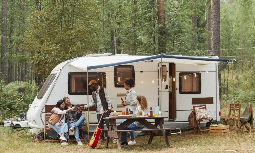 Wide angle view of young people enjoying outdoors while camping with van in forest, copy space