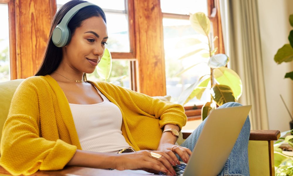 Woman, laptop and remote work, headphones for listening to music while working from home. Female freelancer, copywriter for blog or website with radio or podcast streaming, typing and productivity.