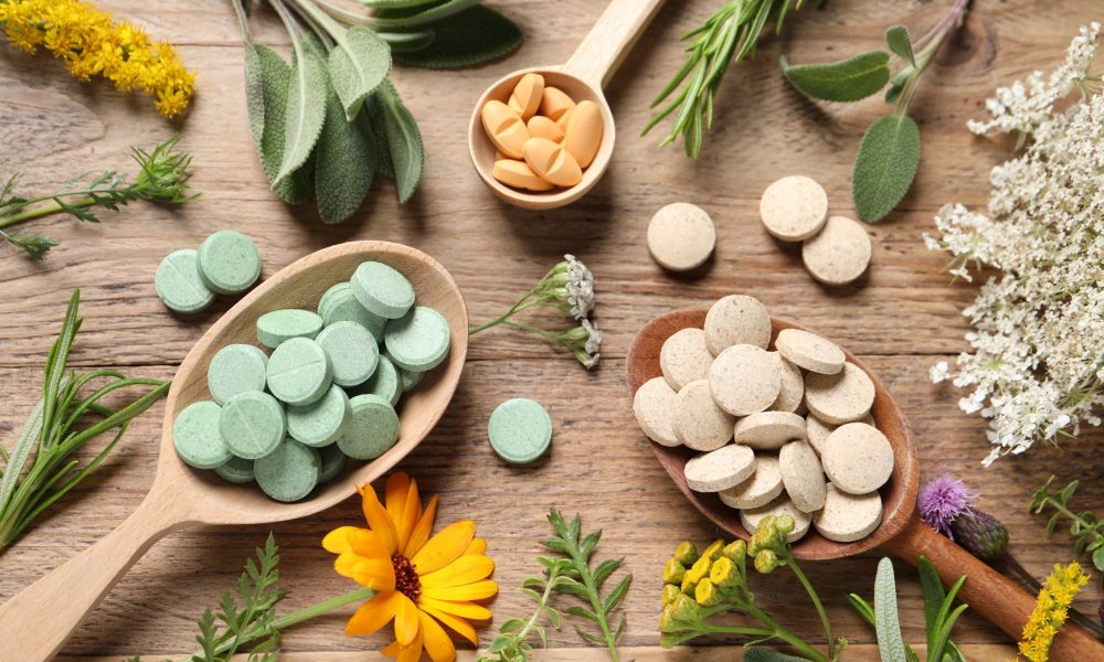 Different pills, herbs and flowers on wooden table, flat lay. Dietary supplements