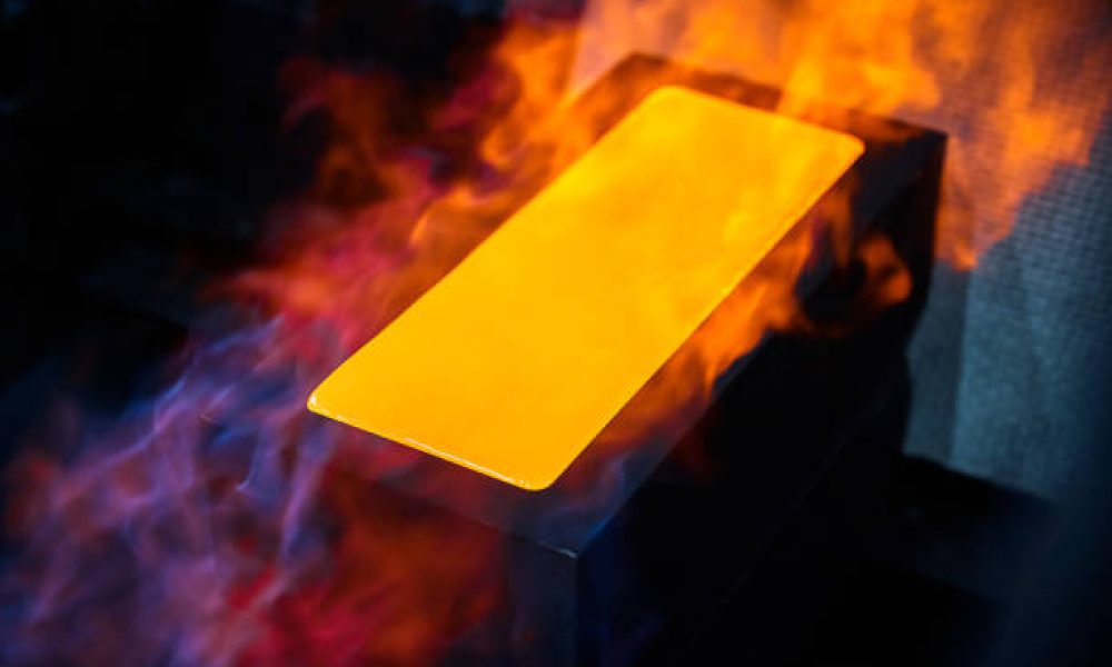 Hot gold ingot chills in graphite casting form on workbench in shielding gases at jewelry production plant extreme close view