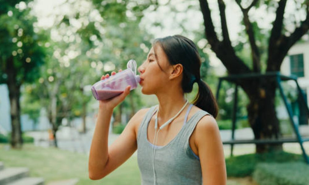 Young Asian female athlete runner drinking protein shake after exercise workout in urban park. Diet and healthy food workout exercise concept.
