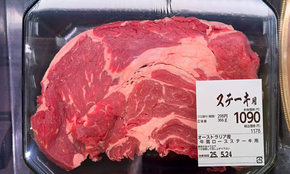 A large cut of raw beef, labeled for steak, is packaged in a clear plastic tray and displayed for sale. The meat is a deep red with visible marbling and streaks of white fat. A white label with Japanese text indicates "オーストラリア産" (Product of Australia) and "牛肩ロース ステーキ用" (Beef Shoulder Loin for Steak). The price is shown as "1090" yen for 366g. The steak is likely on display in a refrigerated section of a grocery store.