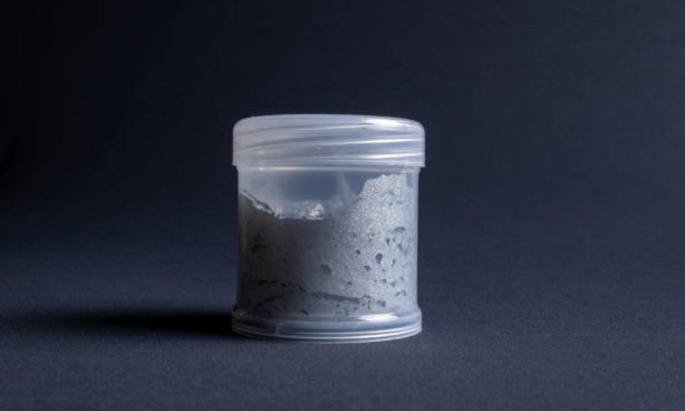 A pot containing resin of a white glitter color on a dark black background. Used for various purposes in industry and at home in the adaptation of furniture and objects for interior decoration.