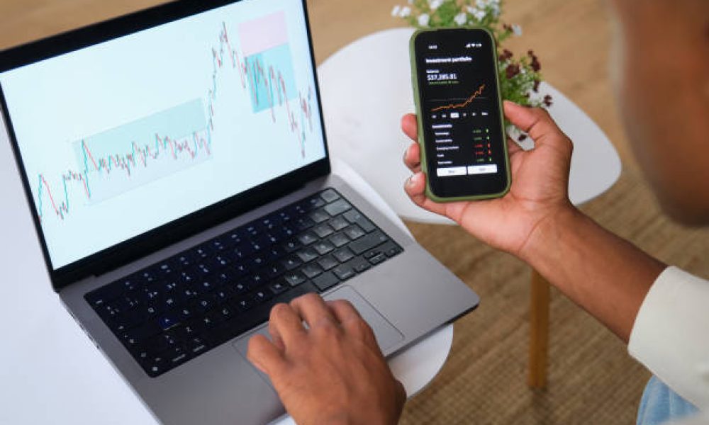 Trader is analyzing charts on his laptop and smartphone app, working remotely from his home office
