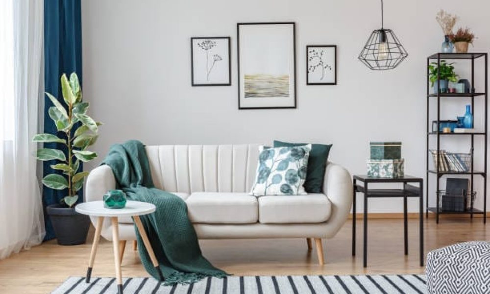 Black table next to sofa with green blanket in cozy apartment interior with gallery of posters