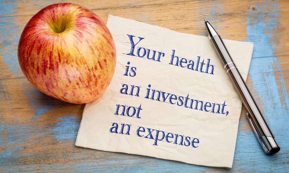 Your health is an investment, not an expense - wellness concept - handwriting on a napkin with a fresh apple